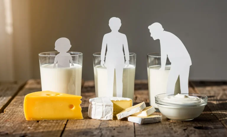 Trois verres de lait et divers produits laitiers sont disposés sur une table en bois devant des silhouettes en papier représentant les âges de la vie.
