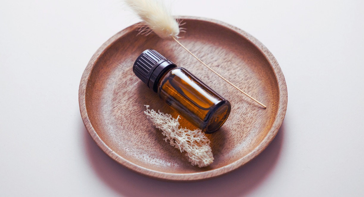 Flacon d'huile essentielle ambrée sur plateau en bois naturel avec plantes séchées, idéal pour diffuseur galet aromathérapie