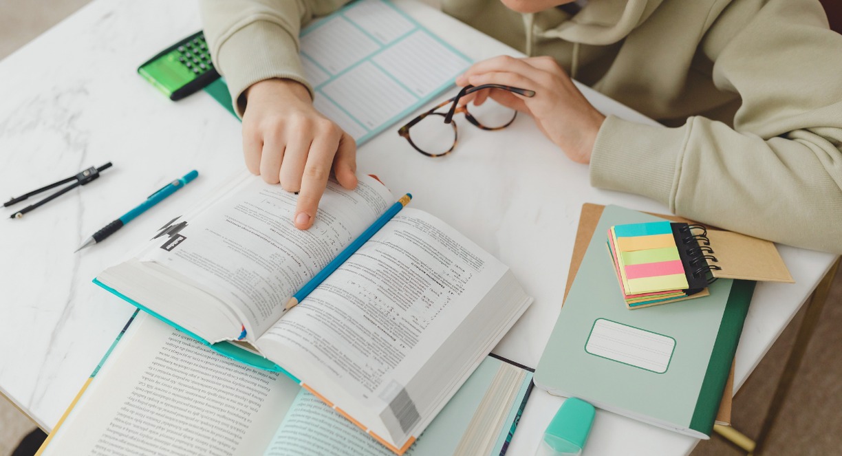 Jeune étudiant feuilletant un livre de cours avec des cahiers et post-its colorés, développement intellectuel et apprentissage