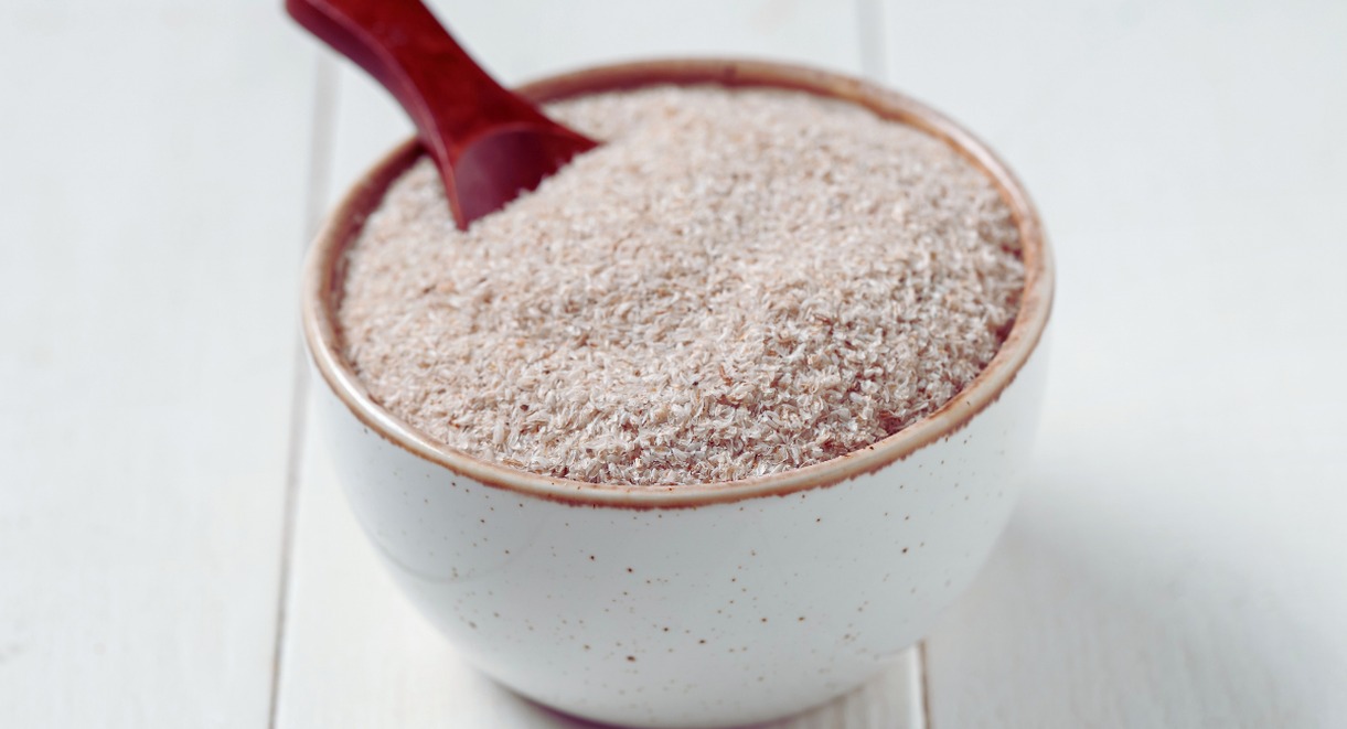 Bol blanc rempli de poudre d'enveloppe de psyllium avec une cuillère rouge, illustrant ce complément alimentaire riche en fibres aux nombreux bienfaits digestifs